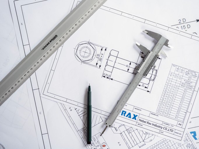 Caliper, pen and ruler lying on top of technical drawing of a bolt