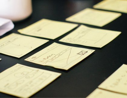 Low-fidelity interface sketches on sticky notes laid out during a UX design and prototyping session for digital process improvement.