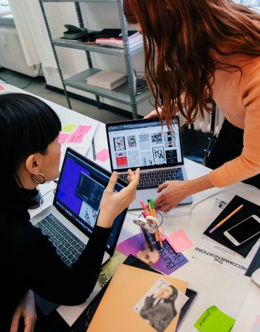 Team members collaborating on laptops during a design sprint session, reviewing digital layouts and creative concepts for user experience development.