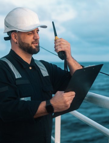 Auditor in maritime shipping checks CO₂ emissions with radio and clipboard – digital auditing processes by Swiss Climate powered by Sclable Workflow Intelligence.