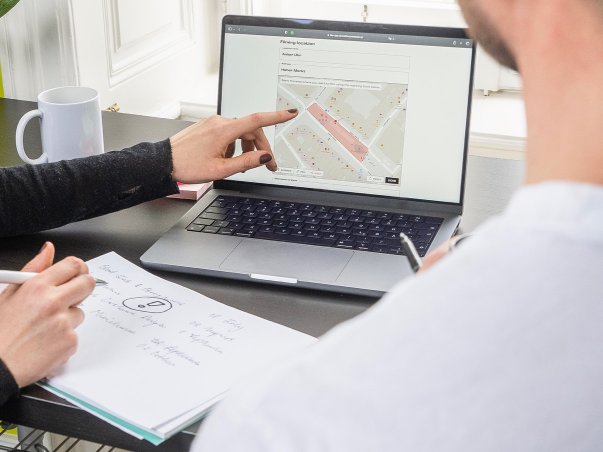 Close-up of woman's hand pointing at map functionality of the Vienna Film Commission online form while making notes