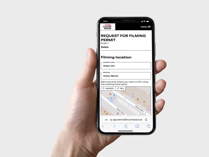 Hand holding a mobile phone which displays the Vienna Film Commmission request-for-filming-permit screen