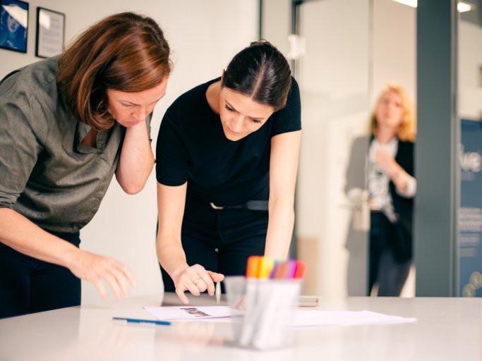 Zwei Frauen beugen sich über einen Tisch und besprechen Notizen während eines Workshops über Kundenanforderungen