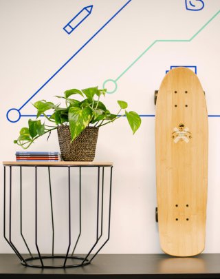 Skateboard propped up against white wall next to coffee table with plant on top