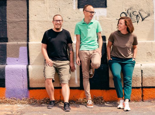 Three sclable team members leaning up against wall covered in street art