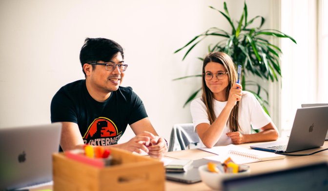 Agile Coach and Developer sitting at table with notebooks and laptops with a plant in the background