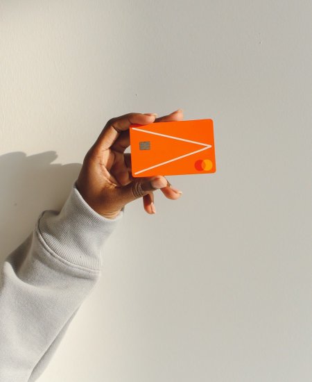 Arm einer Frau, die eine orangefarbene Bankkreditkarte in der Hand hält